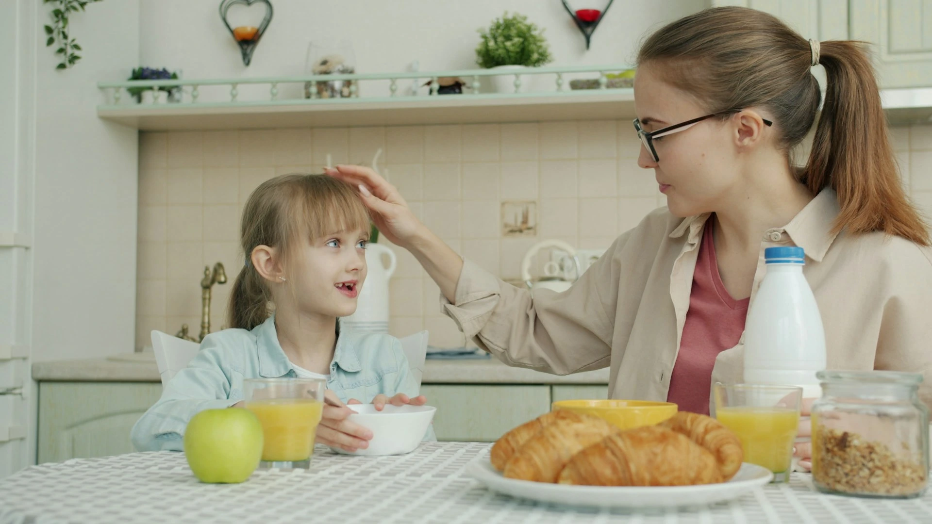 Cinco preguntas para disciplinar con amor paso a paso Mother touches daughter's hair during breakfast.